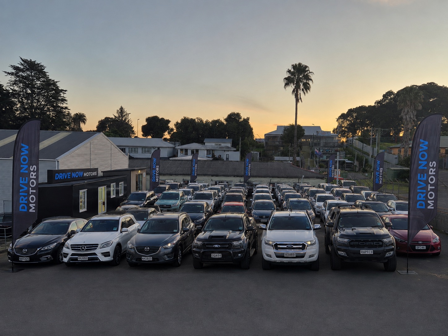 Drive Now Motors forecourt at dusk, full of vehicles for sale